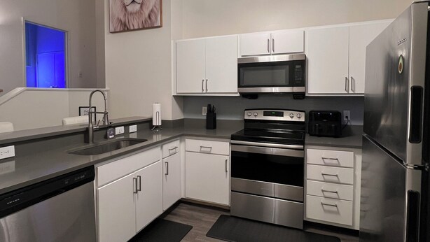 Una cocina moderna con electrodomésticos de acero inoxidable, armarios blancos, microondas, horno y lavavajillas.