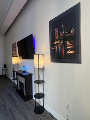 Ein modernes Wohnzimmer mit Flachbildfernseher, zwei Stehlampen, einem gerahmten Stadtbild und einem Kamin.
