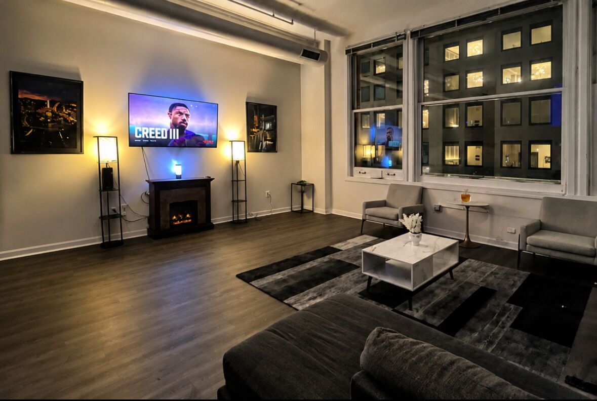 A modern living room with a flat-screen TV, a fireplace, and a large window with multiple panes.