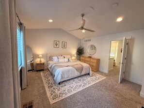 A bedroom with a bed, bedside tables, a ceiling fan, a dresser, a mirror, and a door leading to another room. - The Point Retreat, Theater, Firepit, Near I-15 (Bluffdale)