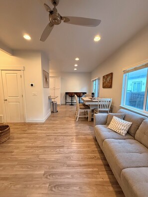 A modern living room with a ceiling fan, a dining area with a table and chairs, and a large window. - The Point Retreat, Theater, Firepit, Near I-15 (Bluffdale)