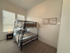 Um quarto com uma cama beliche, uma mesinha de cabeceira com luminária, e duas imagens emolduradas na parede.