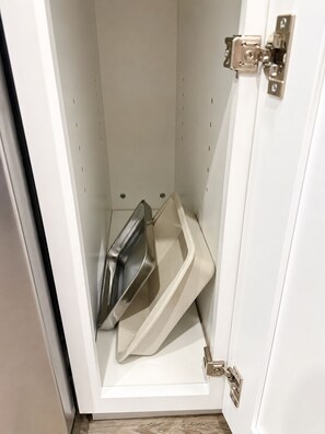 Valkoinen kaappi, jonka sisällä on ruostumattomasta teräksestä valmistettu laite, sekä beigenvärinen alusta ja metallinen salpa.