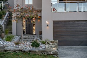 A modern house with a stone staircase, a garage, and a tree with autumn leaves. - Remarkable 5-Bedroom on the Hill (Queenstown)