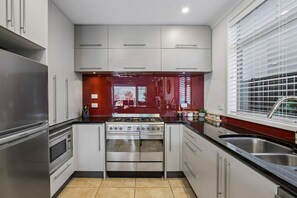 Eine moderne Küche mit Edelstahlgeräten, weißen Schränken und einem großen Fenster mit Jalousien.