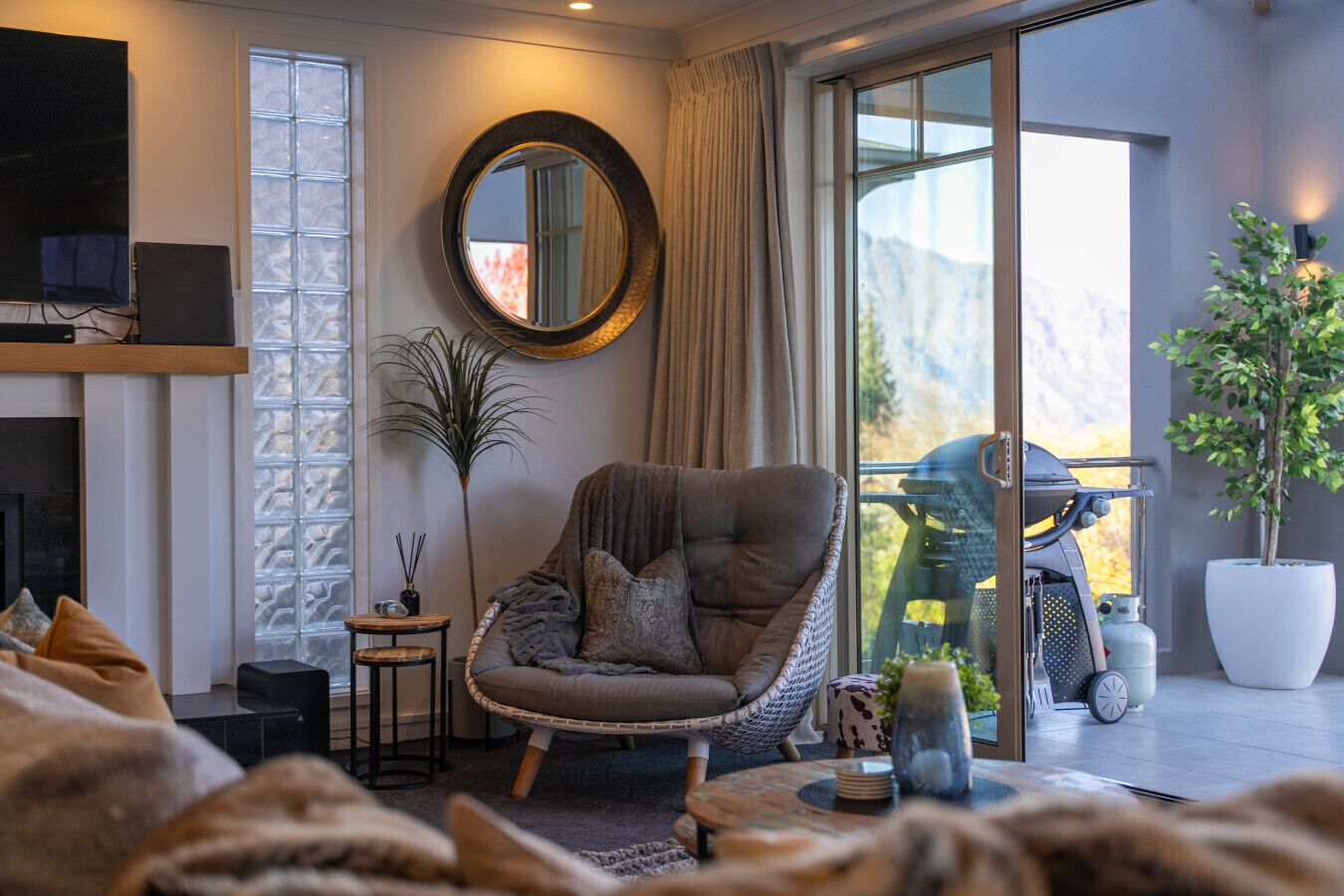 A modern living room with a large window, a round mirror, a comfortable armchair, and a potted plant.