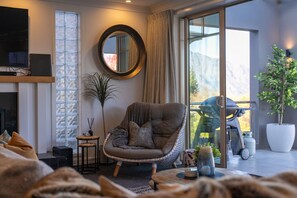 Ein modernes Wohnzimmer mit großem Fenster, einem runden Spiegel, einem bequemen Sessel und einer Topfpflanze.