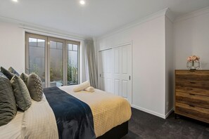 A bedroom with a bed, a dresser, and a window with curtains. - Remarkable 5-Bedroom on the Hill (Queenstown)