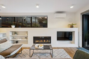 Ein modernes Wohnzimmer mit Kamin, einer Couch, einem Couchtisch und Blick ins Freie.