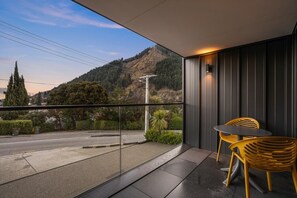 Ein Balkon mit Blick auf eine Straße und Hügel, mit zwei Stühlen und einem Tisch.