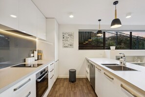 Eine moderne Küche mit weißen Schränken, einer schwarzen Mülltonne und einem Fenster mit Blick auf einen Balkon.