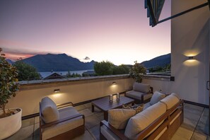 A terrace with outdoor seating, a potted plant, and a view of mountains and a lake. - Remarkable New Home on the Hill (Queenstown)