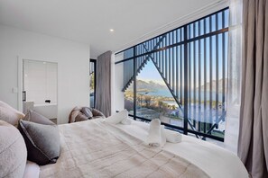 Een moderne slaapkamer met een groot bed, uitzicht op een meer en een trap naar een buitenruimte.
