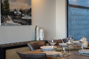 A dining table set with plates, glasses, and cutlery, with a painting and decorative items on the wall. - Remarkable New Home on the Hill (Queenstown)
