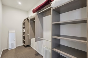 A walk-in closet with open shelving, a radiator, and a door leading to another room. - Remarkable New Home on the Hill (Queenstown)