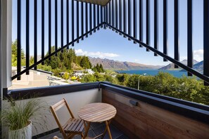 A balcony with a view of a lake and mountains, a wooden chair, and a small table. - Remarkable New Home on the Hill (Queenstown)