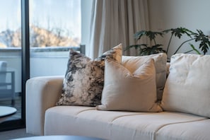 A sofa with three cushions, a plant, and a view of the outdoors through a window. - Remarkable New Home on the Hill (Queenstown)