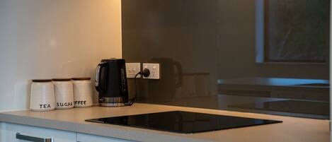 A kitchen with a black induction cooktop, a coffee maker, and labeled containers for tea and sugar.