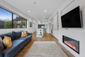 A modern living room with a sofa, TV, fireplace, and kitchen in the background. - Queenstown Quarters - Residence III (Queenstown)