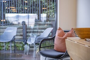 A seating area with wicker chairs and a wooden table, a glass window with a view of outdoor steps and greenery. - Queenstown Quarters - Residence III (Queenstown)