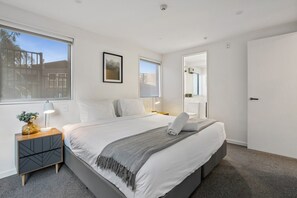 A modern bedroom with a large bed, bedside tables, a window, and a door. - Queenstown Quarters - Residence III (Queenstown)