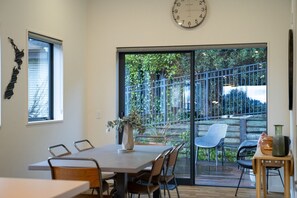 Un comedor con una mesa, sillas, un florero con flores, un reloj y vistas a un jardín a través de un ventanal.