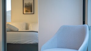 Ett modernt hotellrum med en säng, en stol och en inramad tavla på väggen.