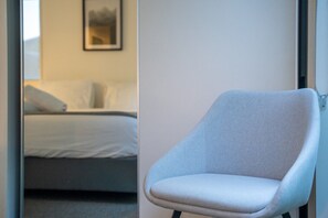A modern hotel room with a bed, a chair, and a framed picture on the wall. - Queenstown Quarters - Residence III (Queenstown)