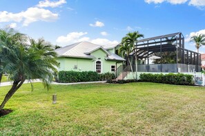 A green house with a covered porch, a lawn, and palm trees. - Min from Naples in Beautiful Brendan Cove w/Private Pool and Covered Courtyard (Bonita Springs)