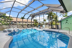 A swimming pool with a glass enclosure, surrounded by lounge chairs and a palm tree. - Min from Naples in Beautiful Brendan Cove w/Private Pool and Covered Courtyard (Bonita Springs)