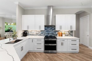 A modern kitchen with white cabinetry, a stainless steel range hood, and a tiled backsplash. - Min from Naples in Beautiful Brendan Cove w/Private Pool and Covered Courtyard (Bonita Springs)
