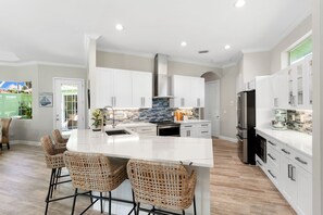 A modern kitchen with white cabinetry, a central island with bar stools, and a backsplash with blue tiles. - Min from Naples in Beautiful Brendan Cove w/Private Pool and Covered Courtyard (Bonita Springs)
