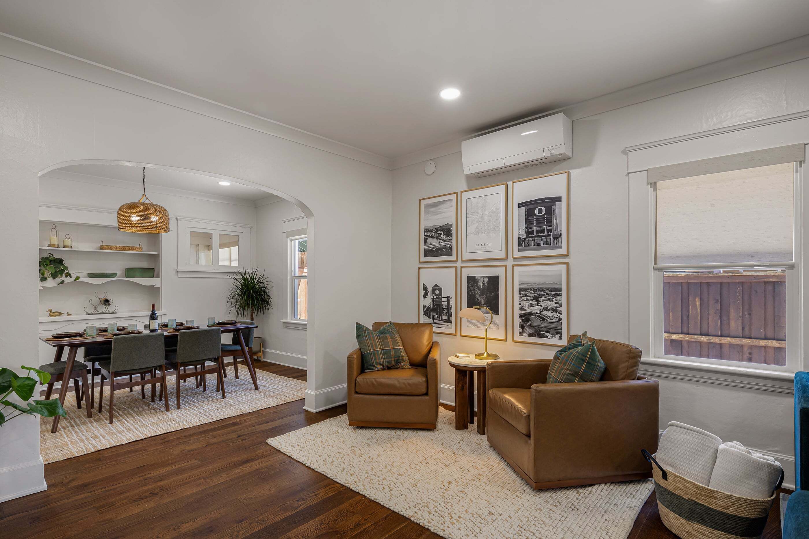 A modern living room with a dining area, featuring a brown leather sofa, a small round table, and a dining table set for four.