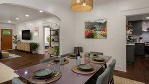 Un comedor con una mesa larga dispuesta para cuatro personas, rodeada de sillas, en una vivienda moderna con cocina al fondo.