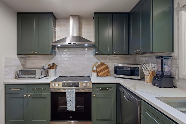 A kitchen with green cabinets, a stainless steel range hood, a microwave, a toaster, and a blender.
