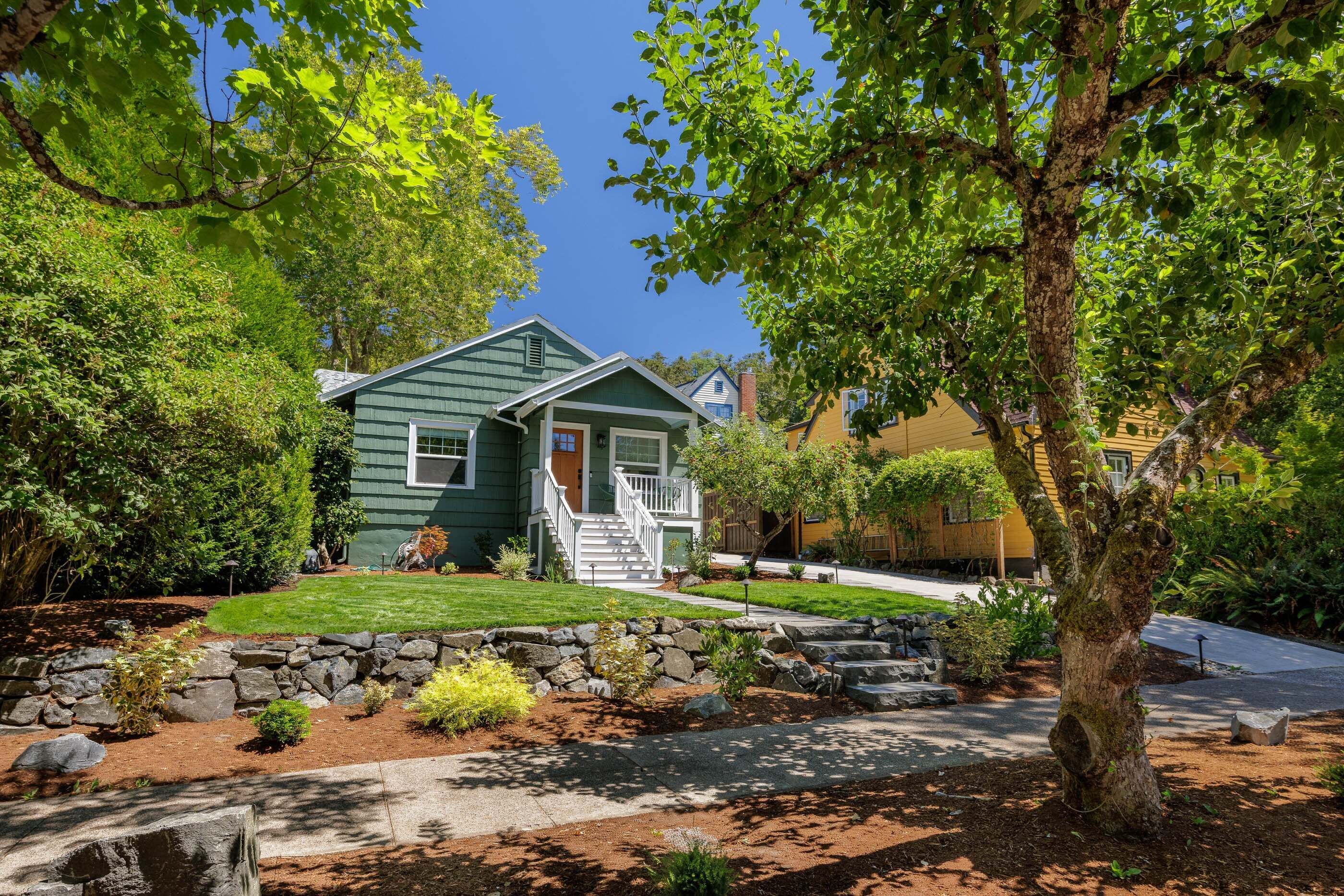 A two-story house with a front porch, surrounded by a stone retaining wall and a well-maintained lawn.