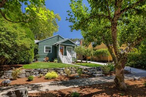 A two-story house with a front porch, surrounded by a stone retaining wall and a well-maintained lawn.