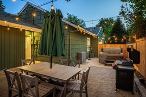 Eine Terrasse im Freien mit Holztisch und -stühlen, einem Grill und Lichterketten.