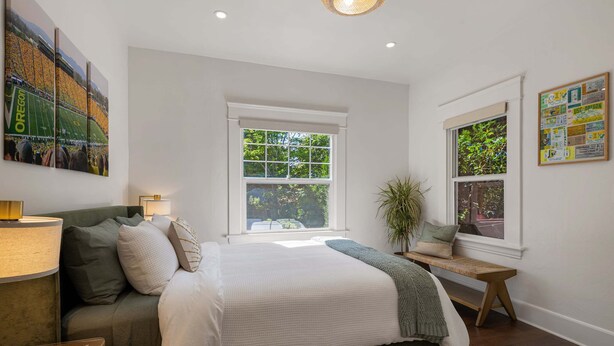 Un dormitorio con cama, ventana, lámpara y una pared con un cartel.