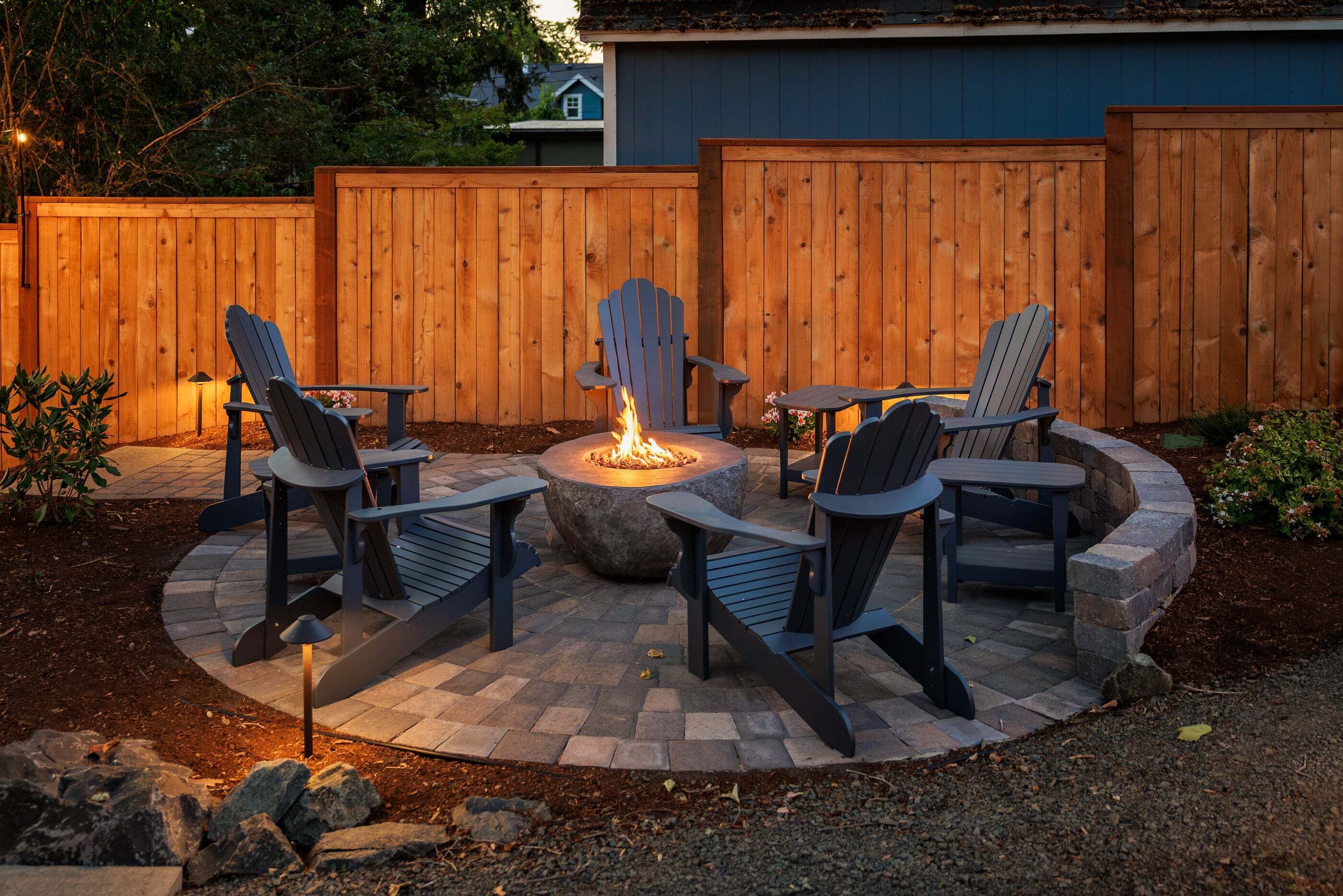 A circular outdoor seating area with Adirondack chairs and a central fire pit.