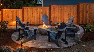 A circular outdoor seating area with Adirondack chairs and a central fire pit.