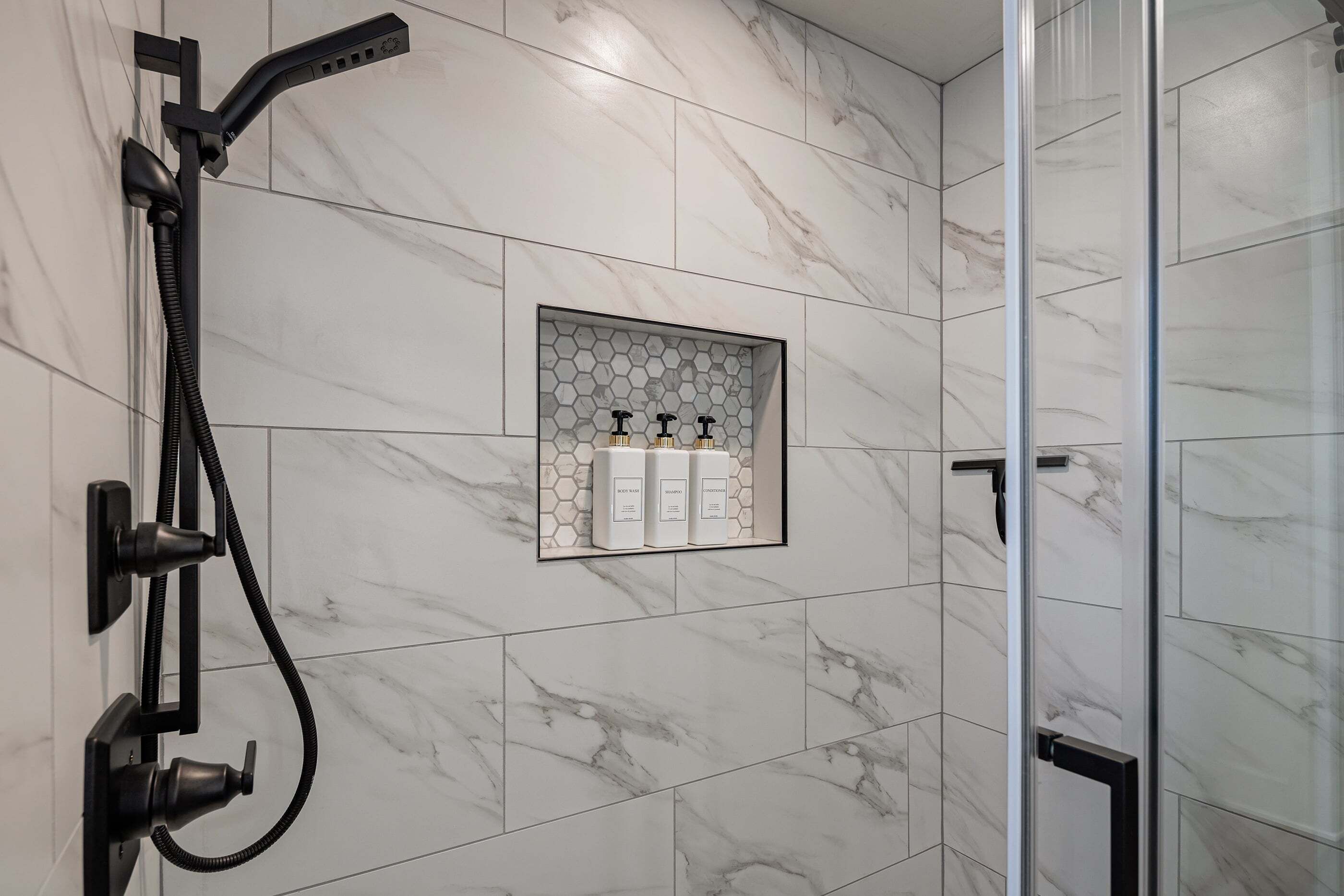 Un baño moderno con ducha, puerta de cristal y estante con artículos de aseo.