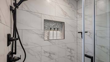 Un baño moderno con ducha, puerta de cristal y estante con artículos de aseo.