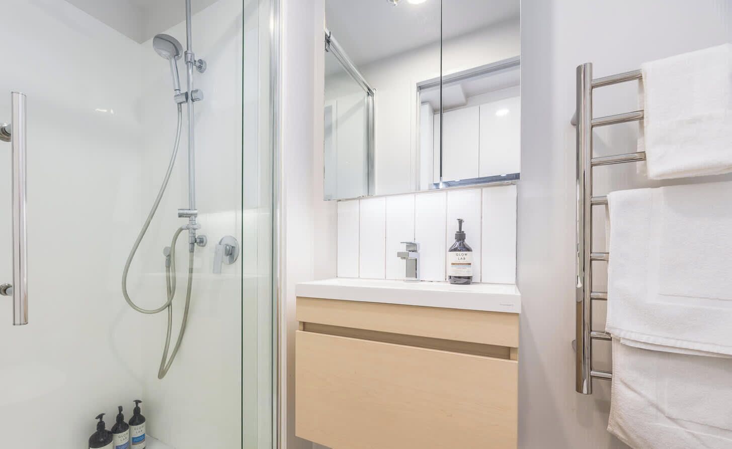 Une salle de bain moderne avec une douche à parois de verre, un meuble-lavabo avec un miroir et un porte-serviettes.