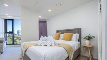 A hotel room with a bed, a window with a view, a bedside table with a plant, and a chair.