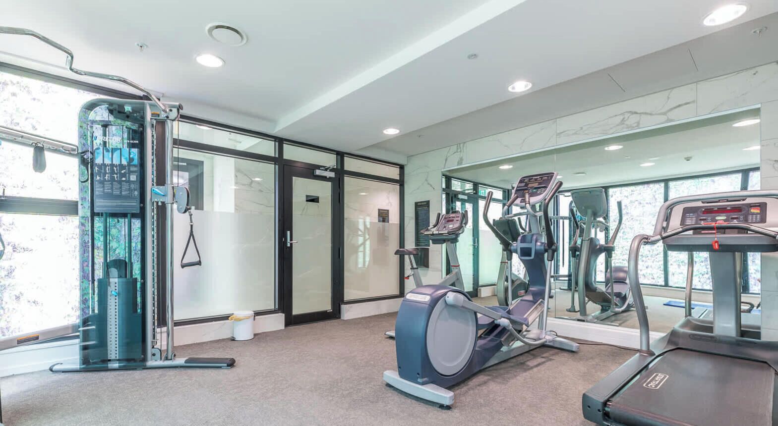 A gym with exercise equipment, a mirrored wall, and a door leading to another room.