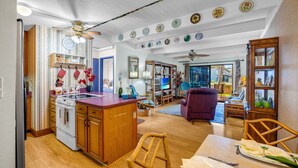 A kitchen with wooden cabinets, a stove, and a dining area with a table and chairs. - Charming Tropical 2BR Condo in Kihei (Kihei)