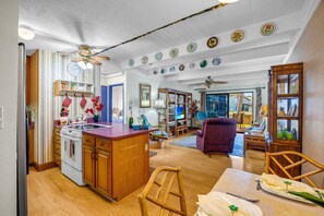 A kitchen with wooden cabinets, a stove, and a dining area with a table and chairs. - Charming Tropical 2BR Condo in Kihei (Kihei)