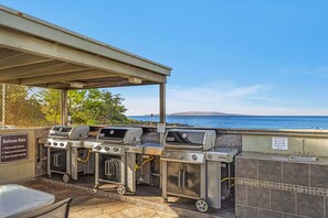 An outdoor barbecue area with multiple grills and a hand washing station, overlooking a scenic view. - Charming Tropical 2BR Condo in Kihei (Kihei)
