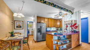 A modern kitchen with wooden cabinets, a central island, and a dining area with chairs. - Charming Tropical 2BR Condo in Kihei (Kihei)